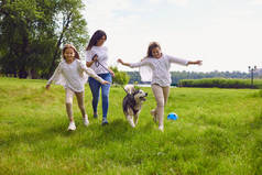 公园里有一只狗的快乐家庭。一位母亲和两个女儿与一只沙哑的狗在大自然的草地上玩耍.