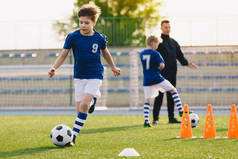 10岁的男孩在跑足球。小学生与年轻教练一起参加足球训练。儿童运动队在训练课上提高运球速度和敏捷性