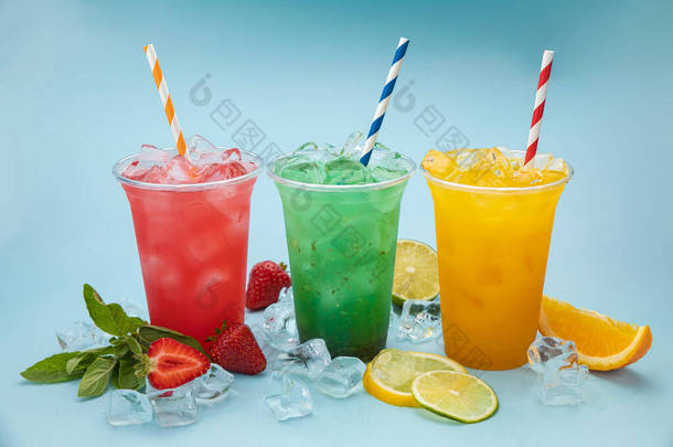 蓝色底色的有冰、水果和浆果的塑料杯子中的<strong>彩色柠檬</strong>水