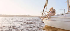 探索梦想。一对快乐的老夫妇坐在平静的蓝色海面上的帆船边。男人抱着他的女人一边欣赏风景