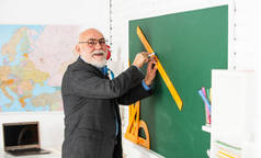 练习时间。戴眼镜的家庭教师在黑板上画有尺子。回学校去你看什么角度。几何形状。高中现代教育。高年级老师画画时使用尺子