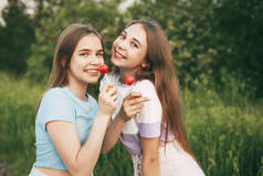 两个快乐的少女拿着一颗鲜红的棒棒糖.