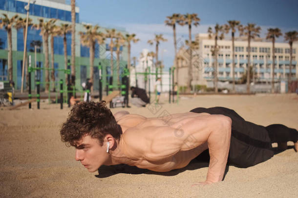 年轻迷人的肌肉男子在海滩上的功能性训练中推举。适合户外运动的人