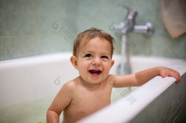 可爱的白种人<strong>宝宝</strong>洗澡，嬉笑着抬起头，躺在浴缸边休息。水花四溅，后面是一个模糊的绿色<strong>浴室</strong>。特写镜头，软焦点