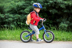 可爱的小孩，带着蓝色头盔，骑着平衡自行车在街上，模糊的背景