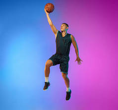 霓虹灯下渐变工作室背景下运动的年轻篮球运动员