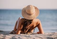 穿着游泳衣和帽子的小女孩坐在海滩上的沙滩上，望着大海。美丽的女士背对着大海，背对着镜头