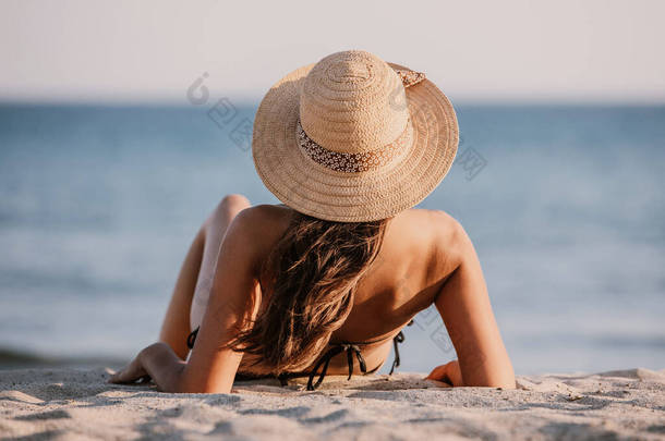 穿着游泳衣和帽子的小女孩坐在海滩上的沙滩上，望着<strong>大海</strong>。美丽的女士背对着<strong>大海</strong>，背对着镜头