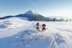 两个小雪人，头戴红帽子，头戴围巾，在雪地上。美丽的冬日落日背景.高山的风景。圣诞快乐，新年快乐.
