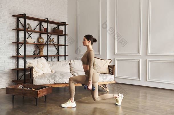 身材苗条的女性老练女子在客厅里用哑铃式的重量做冲刺训练腿。室内,全长,侧视图.运动和身体护理，家庭健康概念.