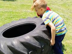 孩子们玩着把轮胎捡起来.孩子游戏中的汽车零部件。一个6岁和7岁的男孩和一个女孩正在草地上做力量训练。头发金黄的人.