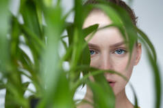 年轻女子肖像。她直视植物的绿叶.自然妆容.