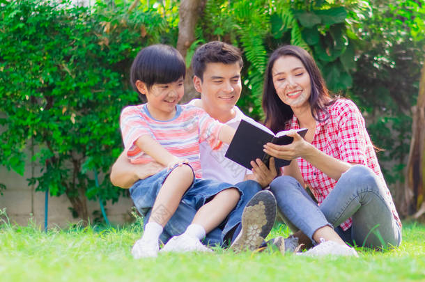 快乐的家庭父亲、母亲和儿子一起在家里的院子里看书。父母与孩子之间的快乐关系或感情纽带享受周末的学习娱乐