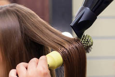 女理发师美容院用吹风机和圆形刷子擦干头发.