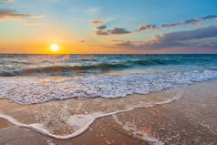 日落时分，天空中带着太阳盘，白云飘扬，白沫浪涌上沙滩，前景广阔.