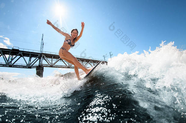 冲浪板上的健美女子在桥的背景下<strong>乘风破浪</strong>而上