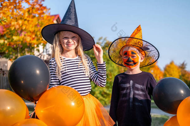 <strong>万圣</strong>节的孩子们哥哥和姐姐穿着<strong>嘉年华</strong>服装在户外.男孩和女孩戴着女巫帽,戴着南瓜糖桶.带着橙色和黑色气球的孩子们真有趣.