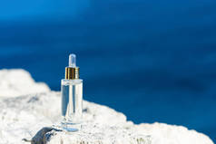 天然石上透明玻璃瓶中的化妆品血清。蓝海背景,自然护肤产品的概念.美丽健康肌肤的瘦身精华