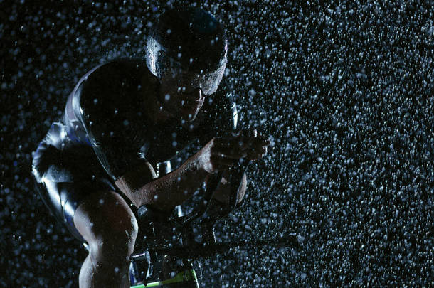 铁人三项全能运动员在夜间骑着职业自行车，天气恶劣，雨下得很大