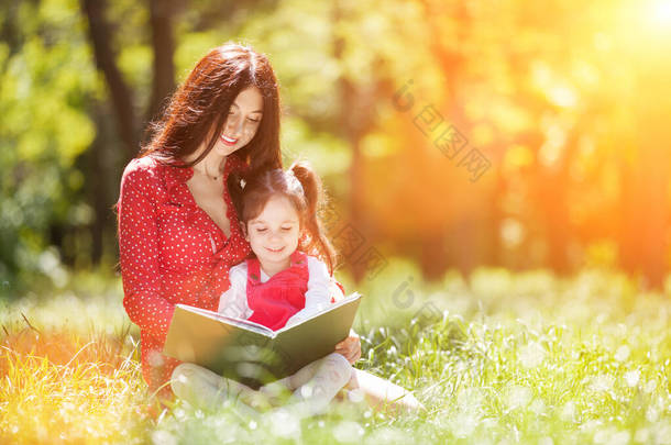 快<strong>乐</strong>的母亲和女儿在夏天的公园里看书。美丽的自然景观与家庭户外生活方式。快<strong>乐</strong>的家庭一起躺在绿草上，拥抱在一起，在户外玩得很<strong>开心</strong>