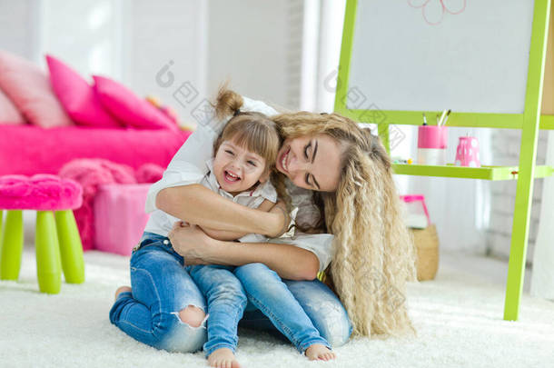 快乐温馨的家庭。母亲和女儿在孩子的房间里。有趣的妈妈和可爱的宝宝在室内玩得很开心。可爱的小女孩在和一个女人玩.