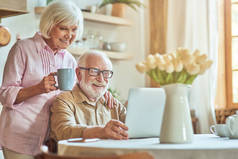 一对快乐的老夫妇在厨房里一起度过早上，一边用笔记本电脑