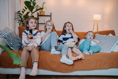 一组5岁至10岁的儿童坐在沙发上看电视，吃爆米花