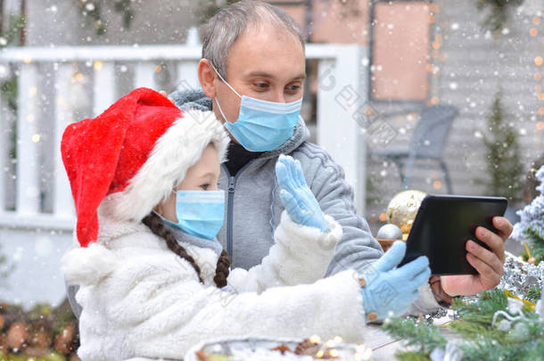 爸爸和女儿戴着防护口罩，头戴圣诞礼帽，通过信使祝圣诞快乐。在检疫期间，安全快乐的新年祝福和快乐的圣诞祝福