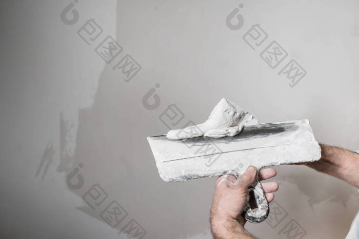 一名建筑工人把白色的油灰放在桶里的铲子上图片-包图网企业站