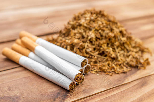一堆堆干切烟草和一堆香烟放在木制桌子上.