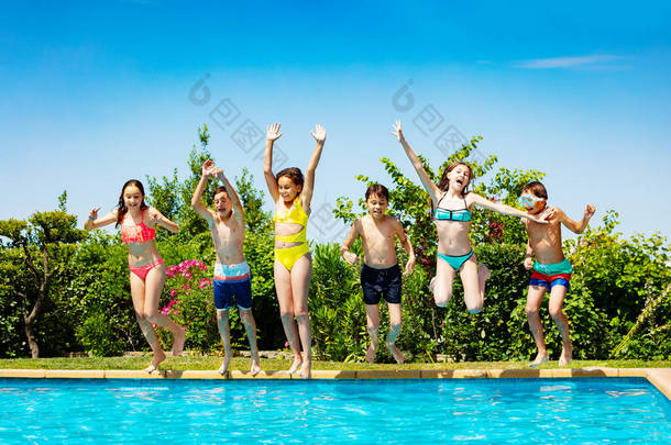 在暑假期间，一群孩子高举双手在外面的游泳池里跳了起来