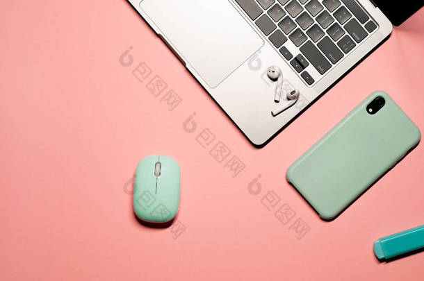 五颜六色的构图，蓝绿色的鼠标，浅蓝色硅盒的智能手机，<strong>银色笔记本</strong>电脑，无线耳机和粉色背景的蓝色标识.