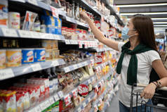 年轻的亚洲女人戴着面具，看着超级市场货架上的商品.