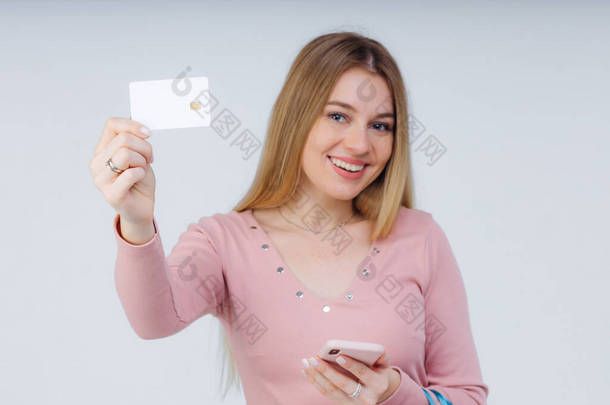 笑的女孩拿着智能手机和<strong>信用卡</strong>。身穿白色背景休闲装的妇女.