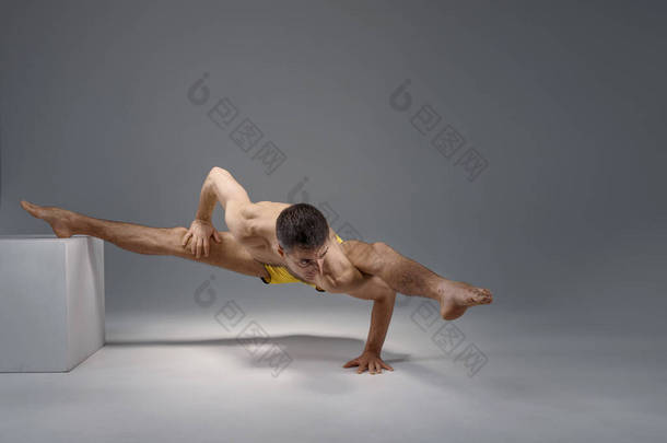 肌体瑜伽在基座上、冥想位置、灰色背景上保持着困难的平衡。强壮的男人做瑜伽运动，体能训练，高度集中精神，健康的生活方式