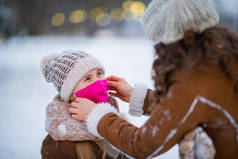 冬季，公园里，穿着针织帽子、头戴医用口罩、头戴针织羊皮外套的优雅的母亲和孩子们站在室外.