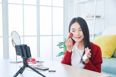 年轻的亚洲女性化妆师、美容师或博主用智能手机记录化妆品化妆指导博客，.