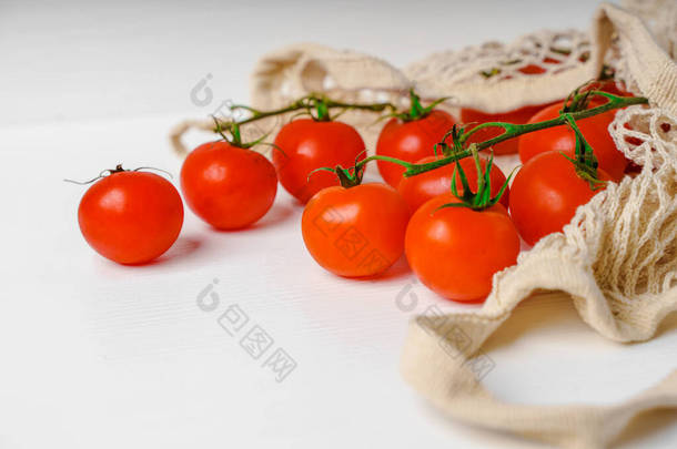 蔬菜在米色的通用网袋里,零废弃物的概念.番茄是鲜红多汁的成熟生态生物,背景为白色.农民的食品市场。马达加斯加包
