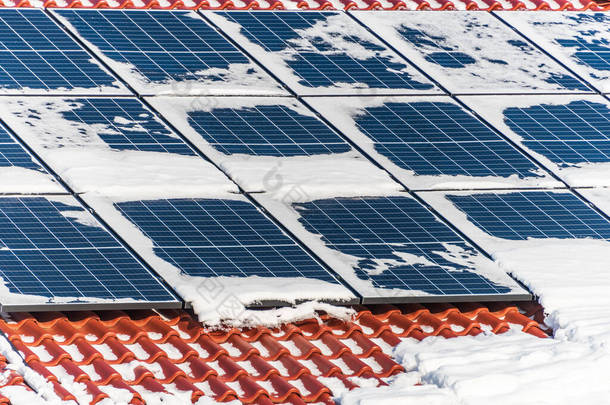 屋顶上覆盖着雪，冬天有太阳能电池板。太阳能发电.冬季在雪地下的光伏太阳能电池板.
