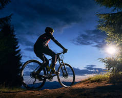骑自行车的人在乌云密布的蓝天下骑自行车的后视镜.夜间山林中骑自行车的男性骑手的轮廓。运动、骑单车和积极休闲的概念.
