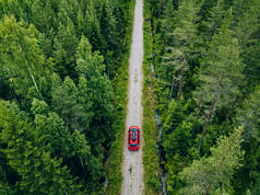 芬兰夏季绿色森林乡间道路上一辆有车架的红色轿车的空中照片