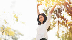 美丽的年轻亚洲女子微笑着举起双手，在自然的阳光下悠闲自在地在公园里享受着复制的空间，享受着片刻、白日梦、无忧无虑和自由的生活理念.
