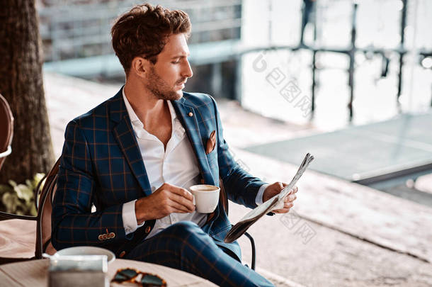 英俊的男人在咖啡馆喝咖啡和看报
