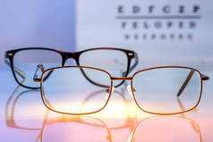 眼镜与处方药镜片背光玻璃桌上的视觉测试与字母在模糊的背景。视力矫正和眼科概念。选定重点