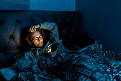 一个沉迷于社交媒体的年轻人在睡觉前检查他的手机，沉迷社交媒体，在黑暗的概念之后