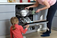 小女孩坐在地板上看着妈妈装洗碗机