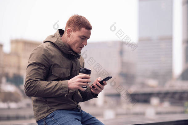 英俊而严肃的男模特写，城市街上的年轻人。年轻人用智能手机，用蓝牙耳机听音乐.