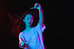 在霓虹灯的黑暗工作室背景上的亚洲年轻女性肖像。人类情感、面部表情、青春、销售、广告的概念.