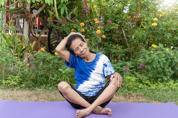 年长的老妇人在户外的瑜伽垫上做伸展运动，以自然的绿色为背景。快乐成熟或年长的女士放松和享受暖身锻炼。健康和健康生活方式概念