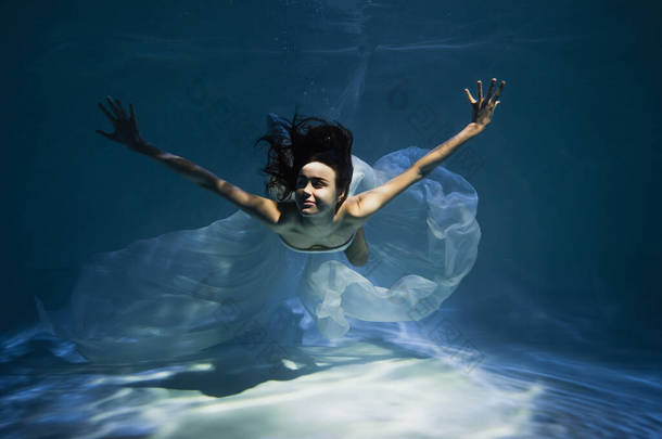 闪烁着微笑的年轻女子穿着洁白典雅的衣服在游泳池里游泳